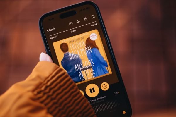 Close-up of a person holding a smartphone displaying an audiobook app.